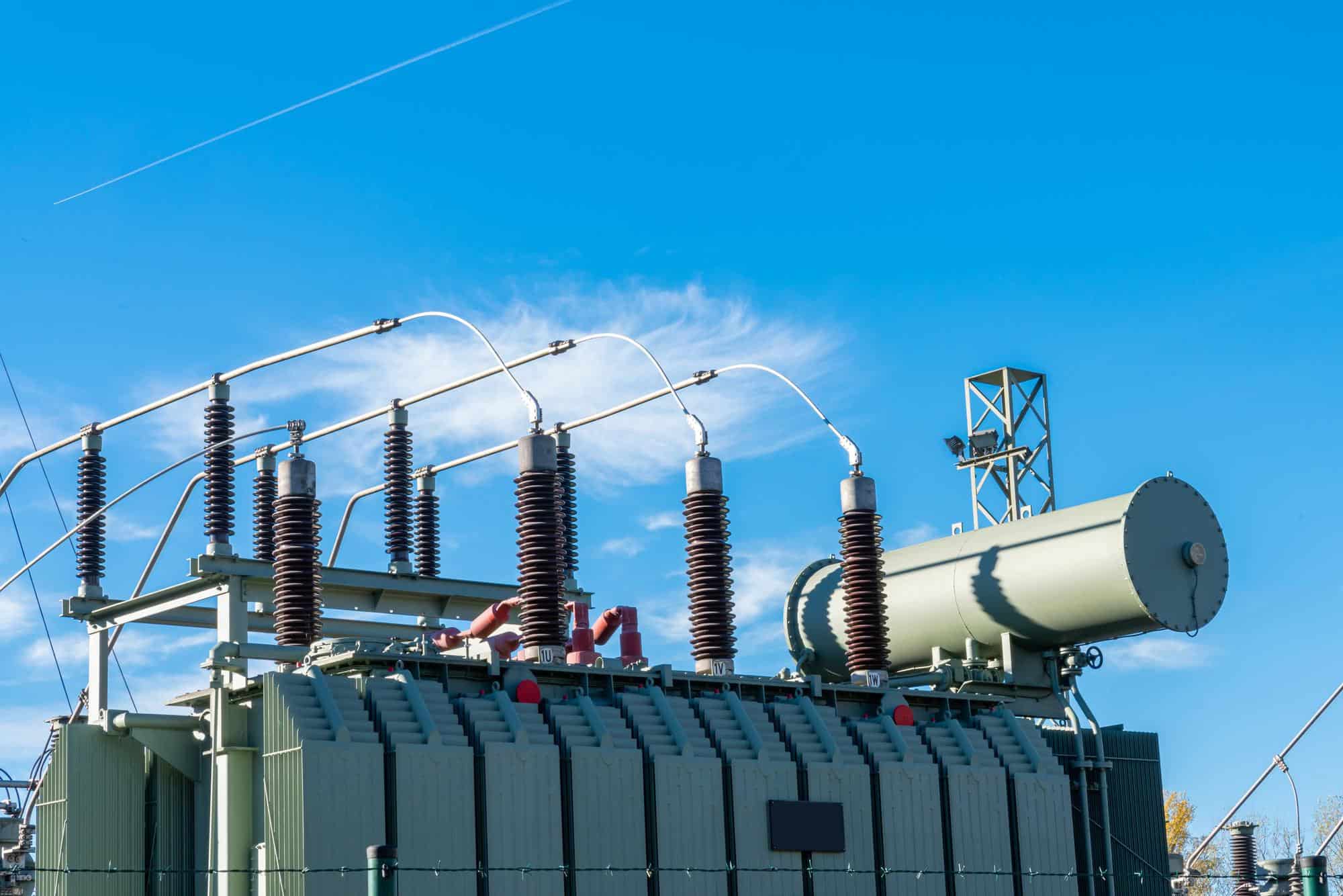 High voltage electrical transformer and insulators under clear blue sky.